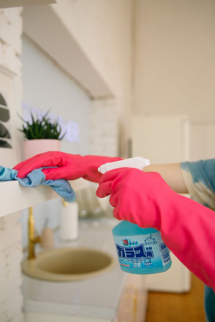 A person is cleaning a kitchen shelf with a spray bottle and cloth, keeping it hygienic and spotless.
